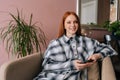 Portrait of happy redhead female using mobile phone sitting in yellow armchair smiling looking at camera. Beautiful red Royalty Free Stock Photo