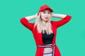 Portrait of happy relaxed beautiful blond young hipster woman in red blouse and cap, standing, holding her head and looking at Royalty Free Stock Photo