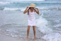 Portrait of a happy Russian little girl in a white dress and hat on a background of the sea. The child walks in the fresh air.