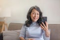 Portrait, Happy 60s retired Asian woman using her phone on a sofa in the living room. chatting, scrolling on the phone Royalty Free Stock Photo