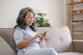 Portrait, Happy 60s retired Asian woman using her phone on a sofa in the living room. chatting, scrolling on the phone Royalty Free Stock Photo