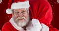 Portrait of happy santa claus carrying bag against maroon background Royalty Free Stock Photo