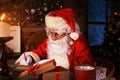 Portrait of happy Santa Claus sitting at his room at home near Christmas tree and answering Christmas letters