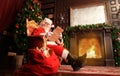 Portrait of happy Santa Claus sitting at his room at home near Christmas tree and reading Christmas letter or wish list. Royalty Free Stock Photo