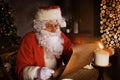 Portrait of happy Santa Claus sitting at his room at home near Christmas tree and reading Christmas letter or wish list Royalty Free Stock Photo