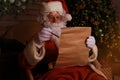 Portrait of happy Santa Claus sitting at his room at home near Christmas tree and reading Christmas letter or wish list Royalty Free Stock Photo