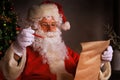 Portrait of happy Santa Claus sitting at his room at home near Christmas tree and reading Christmas letter or wish list Royalty Free Stock Photo