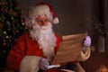 Portrait of happy Santa Claus sitting at his room at home near Christmas tree and reading Christmas letter or wish list Royalty Free Stock Photo