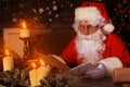 Portrait of happy Santa Claus sitting at his room at home near Christmas tree and reading Christmas letter or wish list Royalty Free Stock Photo