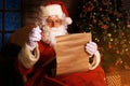 Portrait of happy Santa Claus sitting at his room at home near Christmas tree and reading Christmas letter or wish list Royalty Free Stock Photo