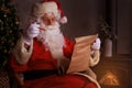 Portrait of happy Santa Claus sitting at his room at home near Christmas tree and reading Christmas letter or wish list Royalty Free Stock Photo