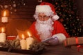 Portrait of happy Santa Claus sitting at his room at home near Christmas tree and reading Christmas letter or wish list Royalty Free Stock Photo