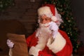 Portrait of happy Santa Claus sitting at his room at home near Christmas tree and reading Christmas letter or wish list Royalty Free Stock Photo