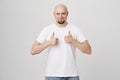 Portrait of happy satisfied bald bearded guy showing thumbs up and smiling, being pleased with item he bought, standing