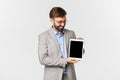 Portrait of happy and satisfied businessman in gray suit and glasses, looking and showing digital tablet screen, smiling Royalty Free Stock Photo