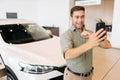 Portrait of happy satisfied buyer male client doing selfie picture on smartphone at dealership after bought new car