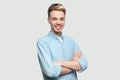 Portrait of happy satisfied handsome young man in light blue shirt standing with crossed arms and looking at camera with toothy Royalty Free Stock Photo