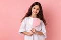 Happy satisfied little girl holding paper pink heart on stick and smiling to camera, sharing love.