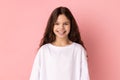 Satisfied little girl in T-shirt looking at camera with toothy smile, expressing positive expression