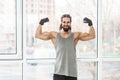 Portrait of happy satisfied sporty young adult muscular trainer man with curly long hair standing with raised heavy arms, showing