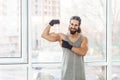 Portrait of happy satisfied young adult muscular man with curly long hair standing with raised heavy arms, pointing finger on