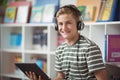 Portrait of happy schoolboy listening music while using digital tablet in library Royalty Free Stock Photo