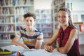 Portrait of happy schoolgirl sitting with her classmate in library