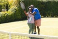Portrait of happy senior african american couple with rackets embracing on sunny grass tennis court Royalty Free Stock Photo