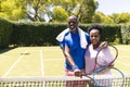 Portrait of happy senior african american couple with tennis rackets embracing on sunny grass court Royalty Free Stock Photo