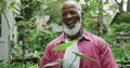 Portrait of happy senior african american man holding plants and similing in garden