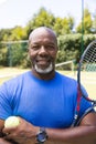 Portrait of happy senior african american man with tennis racket and ball at sunny grass court Royalty Free Stock Photo