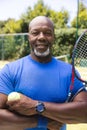 Portrait of happy senior african american man with tennis racket and ball at sunny grass court Royalty Free Stock Photo