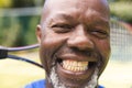 Portrait of happy senior african american man with tennis racket at sunny grass court Royalty Free Stock Photo