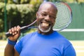 Portrait of happy senior african american man with tennis racket at sunny grass court Royalty Free Stock Photo