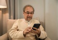 Portrait of happy senior Asian man wearing glasses sitting using technology smartphone with application in living room at home Royalty Free Stock Photo