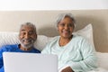 Portrait of happy senior biracial couple lying in bed and using laptop at home Royalty Free Stock Photo