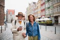 Portrait of happy senior couple tourists smiling, holding hands, using smartphone outdoors in historic town Royalty Free Stock Photo