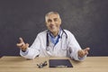 Portrait of happy senior male doctor sitting at desk, looking at camera and smiling Royalty Free Stock Photo