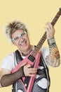 Portrait of happy senior male punk rock musician playing guitar over yellow background Royalty Free Stock Photo