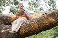 portrait happy senior man sitting and reading a book on tree trunk in summer park Royalty Free Stock Photo