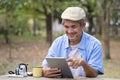 portrait happy senior man using online internet tablet searching direction for his journey while resting in the national park Royalty Free Stock Photo