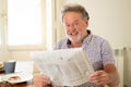Happy old man reading the newspaper while having breakfast Royalty Free Stock Photo