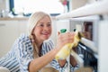 Portrait of senior woman cleaning kitchen cabinet doors indoors at home. Royalty Free Stock Photo