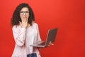 Portrait of happy shocked surprised woman standing with laptop computer isolated on red background