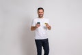 Portrait of happy shopaholic man with credit card making mobile payment against white background