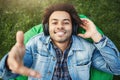 POrtrait of happy sincere smiling african-american student lying on bean bag chair and stretching hand at camera while Royalty Free Stock Photo