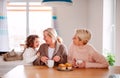 A portrait of small girl with mother and grandmother at the table at home. Royalty Free Stock Photo