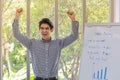 Portrait of happy smart young asian businessman clench two fists and emotion glad with meeting board with sale chart in office