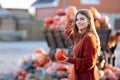 Portrait of happy smile woman with small pumpkin in hand near wooden wagon with pumpkin on farmers market in brown sweater, dress Royalty Free Stock Photo