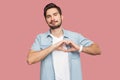 Portrait of happy smiley handsome bearded young man in blue casual style shirt standing with love hand gesture on heart and Royalty Free Stock Photo